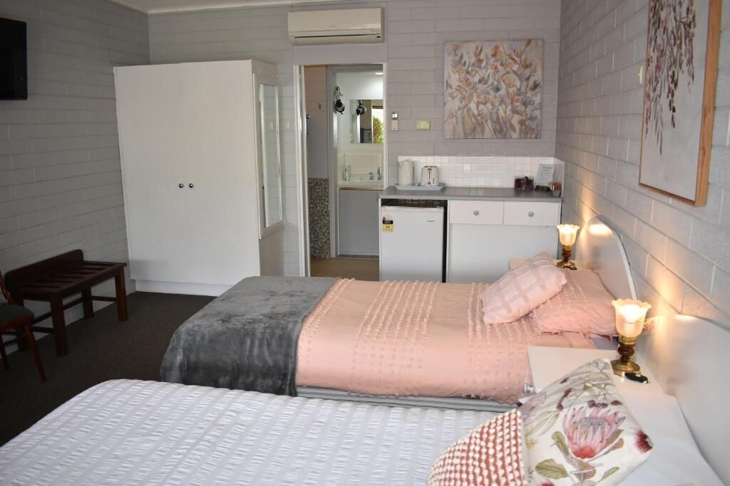 A hotel room with a bed, bedside table, and a small kitchenette area.