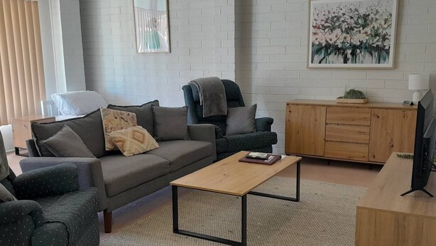 Una sala de estar moderna con un sofá gris, una mesa de centro de madera y un televisor sobre un mueble de madera.