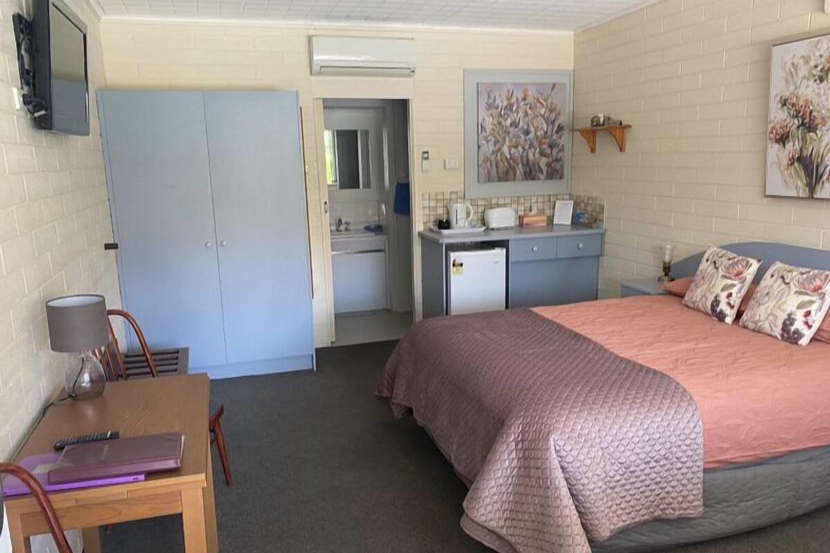 A compact room with a bed, a desk, a chair, a kitchenette, and a bathroom.
