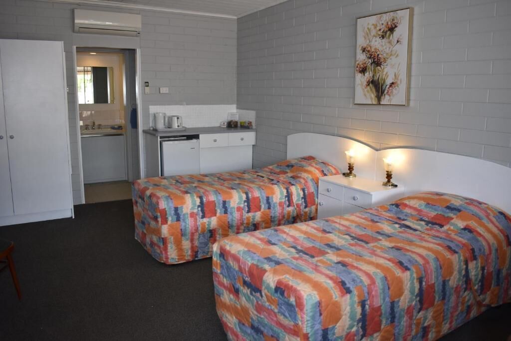 Habitación de hotel con dos camas, un escritorio, una silla y una kitchenette.