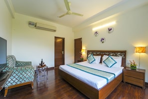 A hotel room with a large bed, a desk, a chair, a ceiling fan, and a wall-mounted air conditioner. - Kalmia Kasauli 3BHK Villa : King sized bed +Bonfire +WiFi+ Cook (Kasauli)