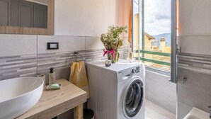 A modern bathroom with a large sink, a washing machine, and a window with a view of buildings.