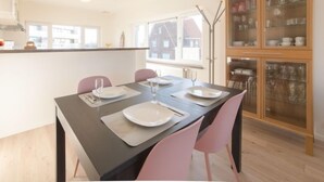 A dining area with a table set for two, pink chairs, and a cabinet with glass doors containing dishes. - De Zeegloed duplex with parking by Interhome (De Haan)
