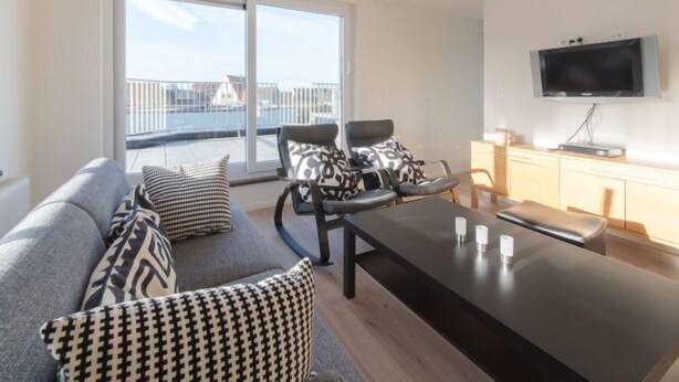 A modern living room with a sofa, armchairs, a coffee table, and a TV. - De Zeegloed duplex with parking by Interhome (De Haan)