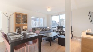 A modern living room with a dining area, a sofa set, a wooden cabinet, and large windows. - De Zeegloed duplex with parking by Interhome (De Haan)