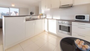 A modern kitchen with white cabinets, a stainless steel oven, a microwave, and a black dining table with a bowl of fruit. - De Zeegloed duplex with parking by Interhome (De Haan)