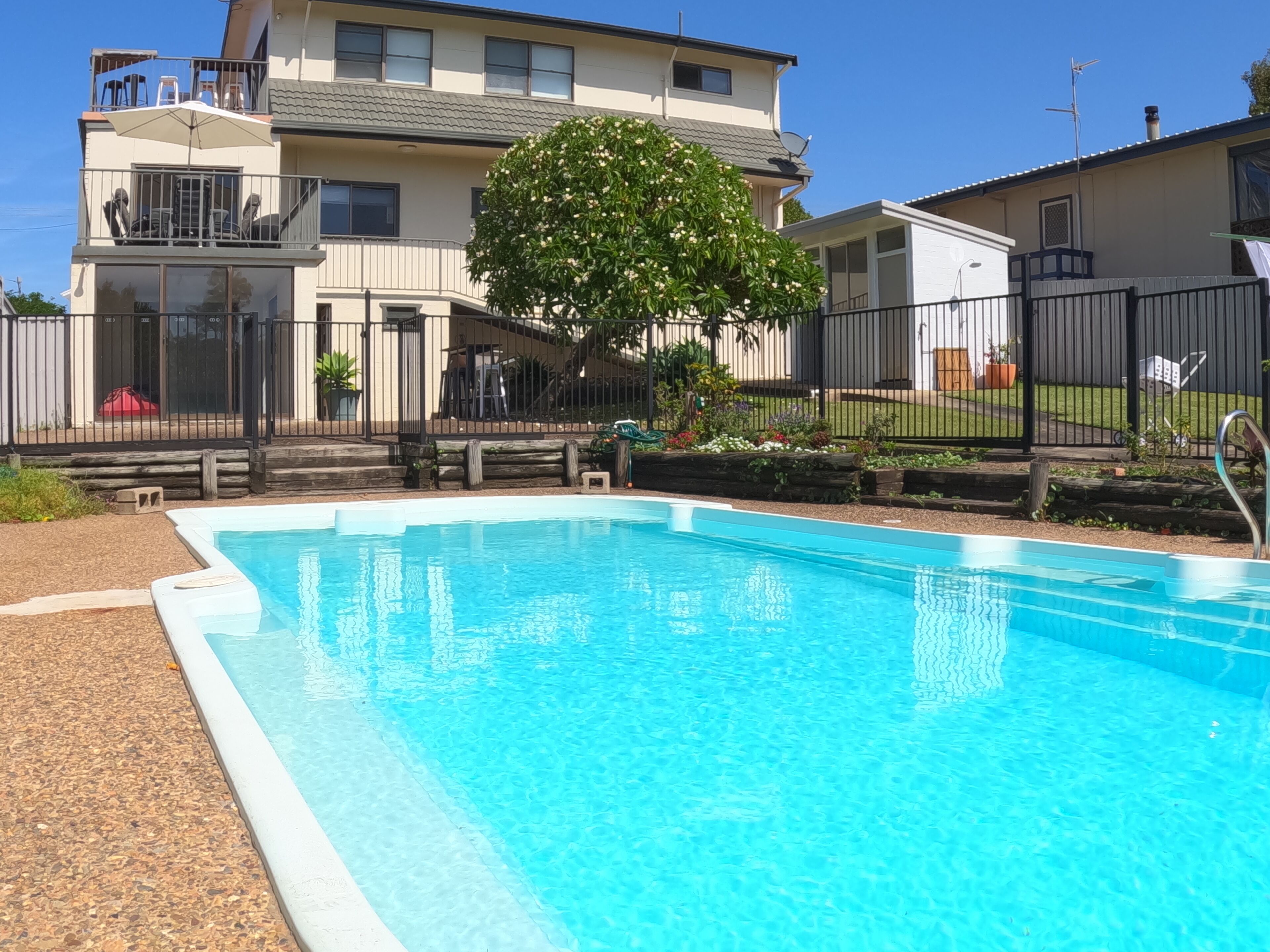 A swimming pool with a clear blue water surface, surrounded by a fence and a building with balconies and windows.