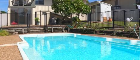 A swimming pool with a clear blue water surface, surrounded by a fence and a building with balconies and windows.