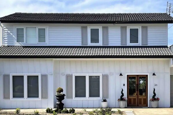 Un bâtiment blanc à deux étages, doté d’un toit en tuiles, de nombreuses fenêtres et d’une porte sur laquelle est inscrit le numéro « 26 » sur le côté droit.