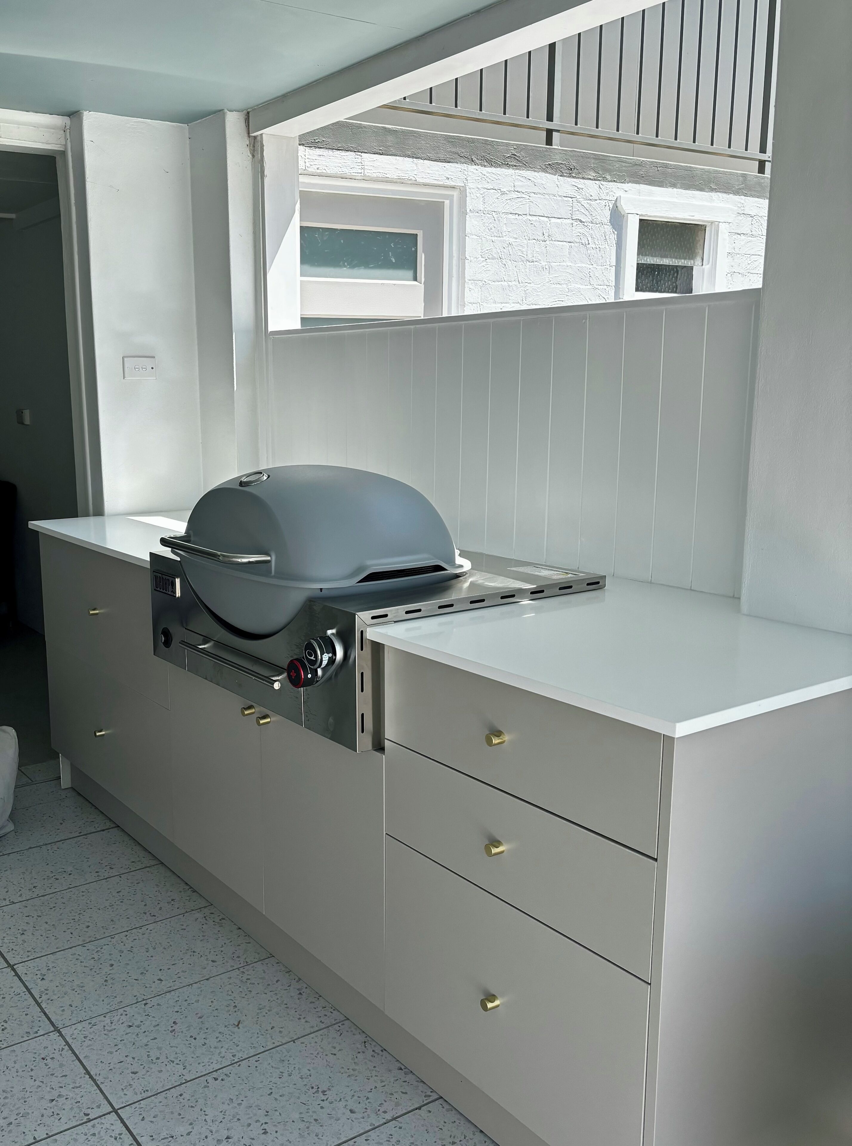 A modern kitchen with a built-in grill, white cabinetry, and a window above the sink.