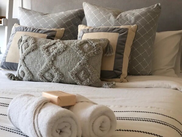 A neatly made bed with rolled white towels, a wooden soap bar, and patterned pillows. - Modern Farmhouse at Pacific Sands Mollymook Beach (Mollymook Beach)