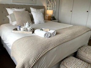 Un lit bien fait, avec des draps blancs, un plaid beige en tricot et des serviettes enroulées.