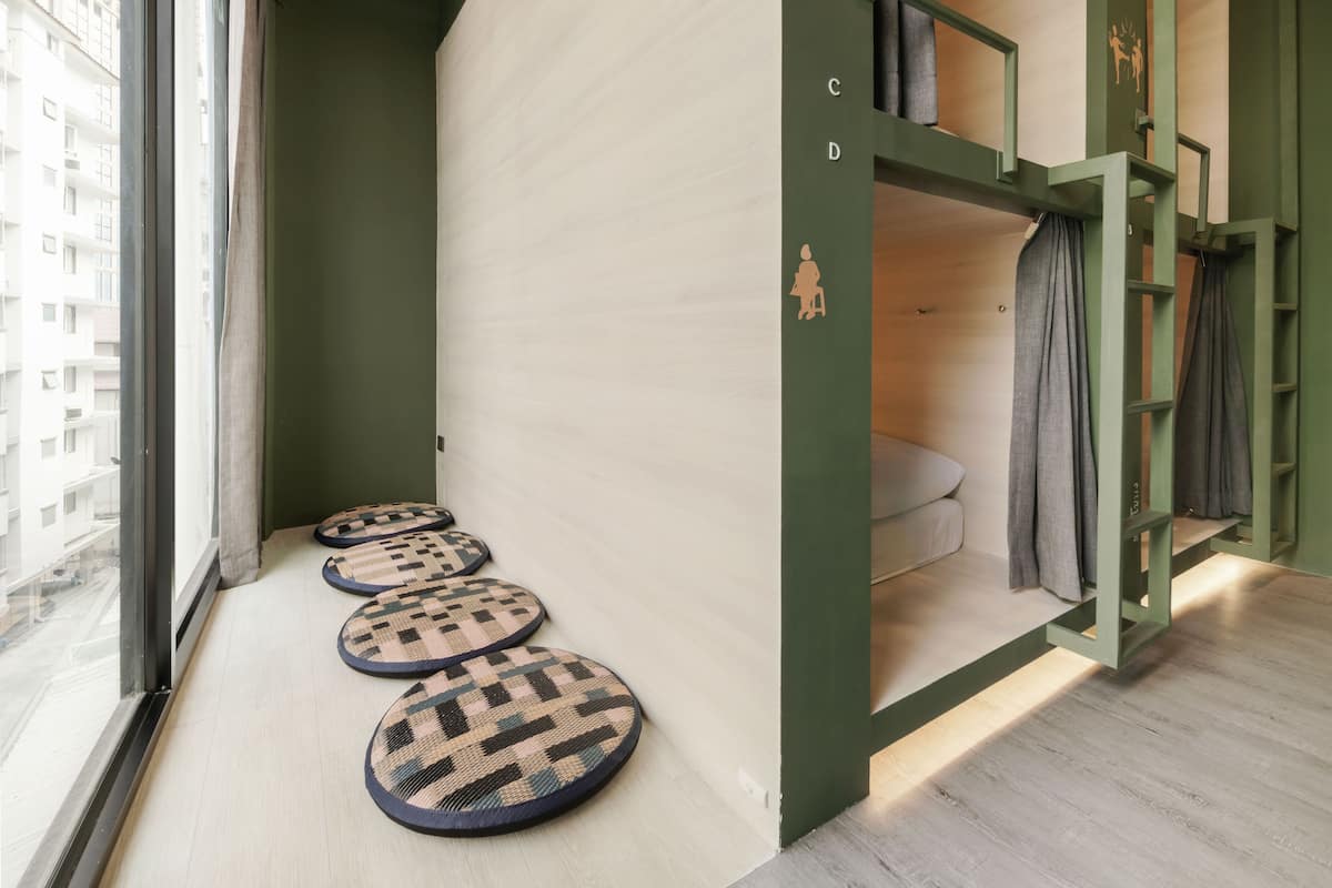 Una habitación con ventana, pared verde, suelo de madera y una cama litera con cortina.