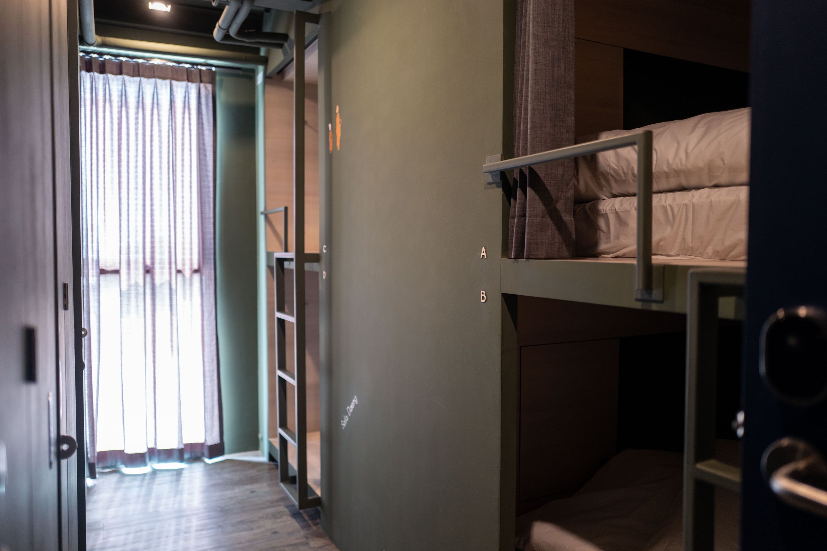A narrow hallway with bunk beds on one side and a door leading to a room with a bed.