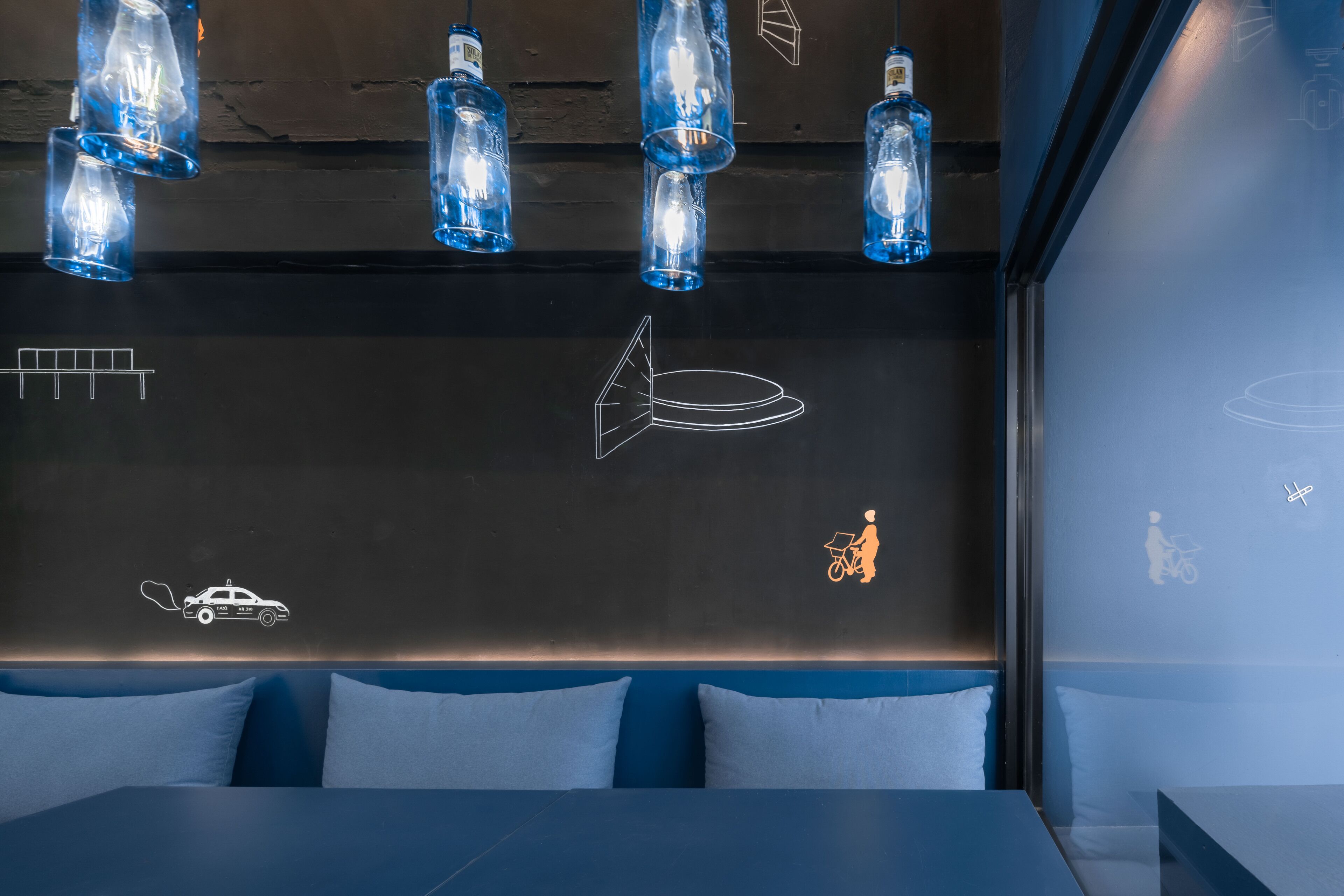 A modern hotel room with a dark wall, a blue sofa, and a bed. There are wall decals of a car, a bicycle, and a rocket.