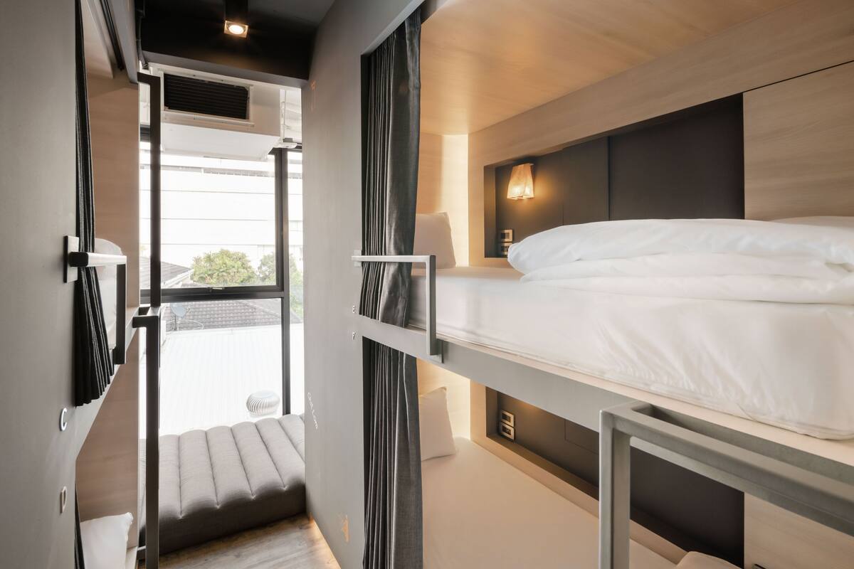 Habitación de hotel moderna con literas, un pequeño rincón de descanso y vistas al exterior.