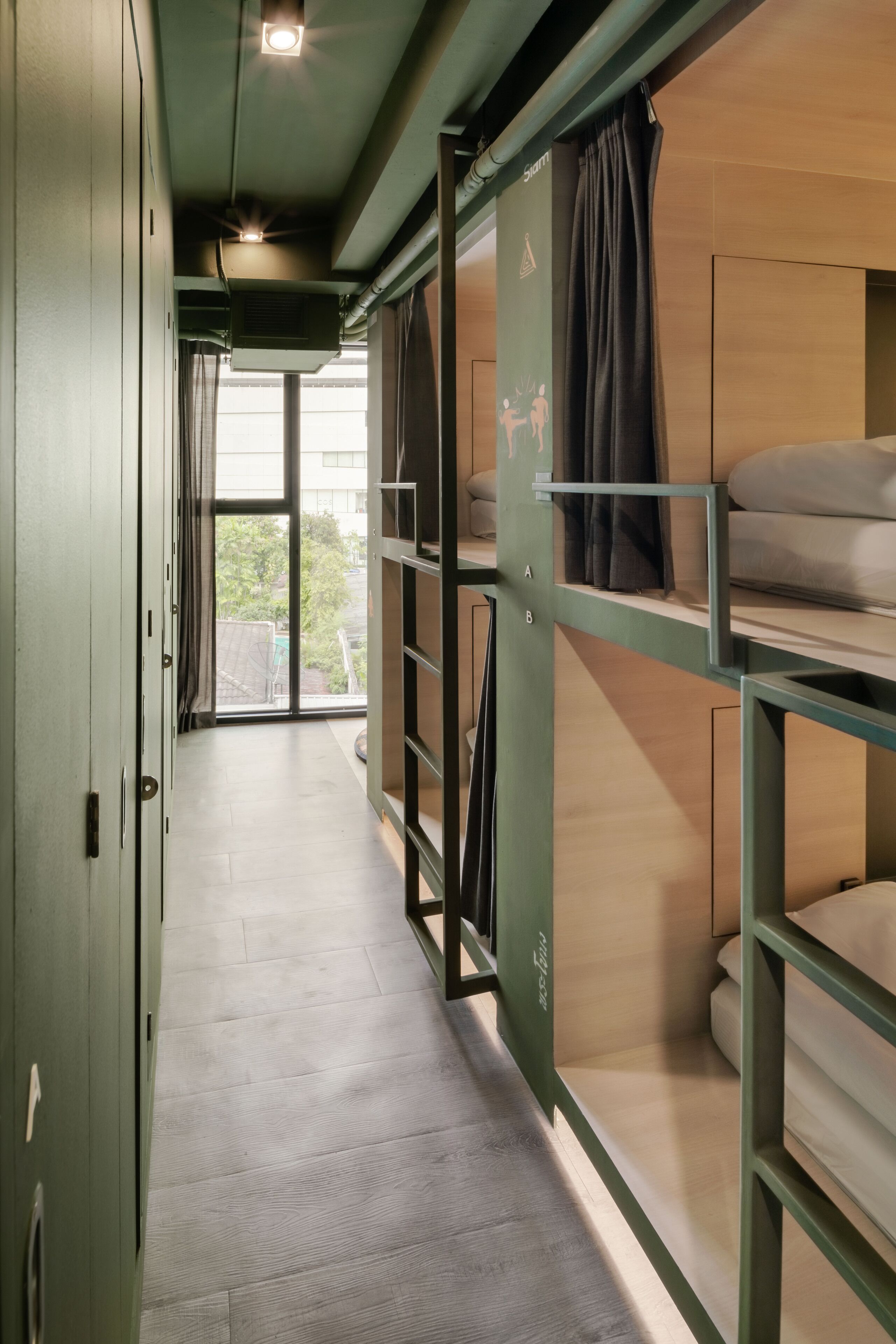 A narrow corridor with bunk beds on the right, a door on the left, and a window at the end.