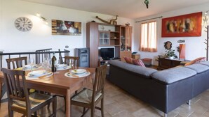 A dining area with a wooden table set for four, a sofa, and a television in the background.