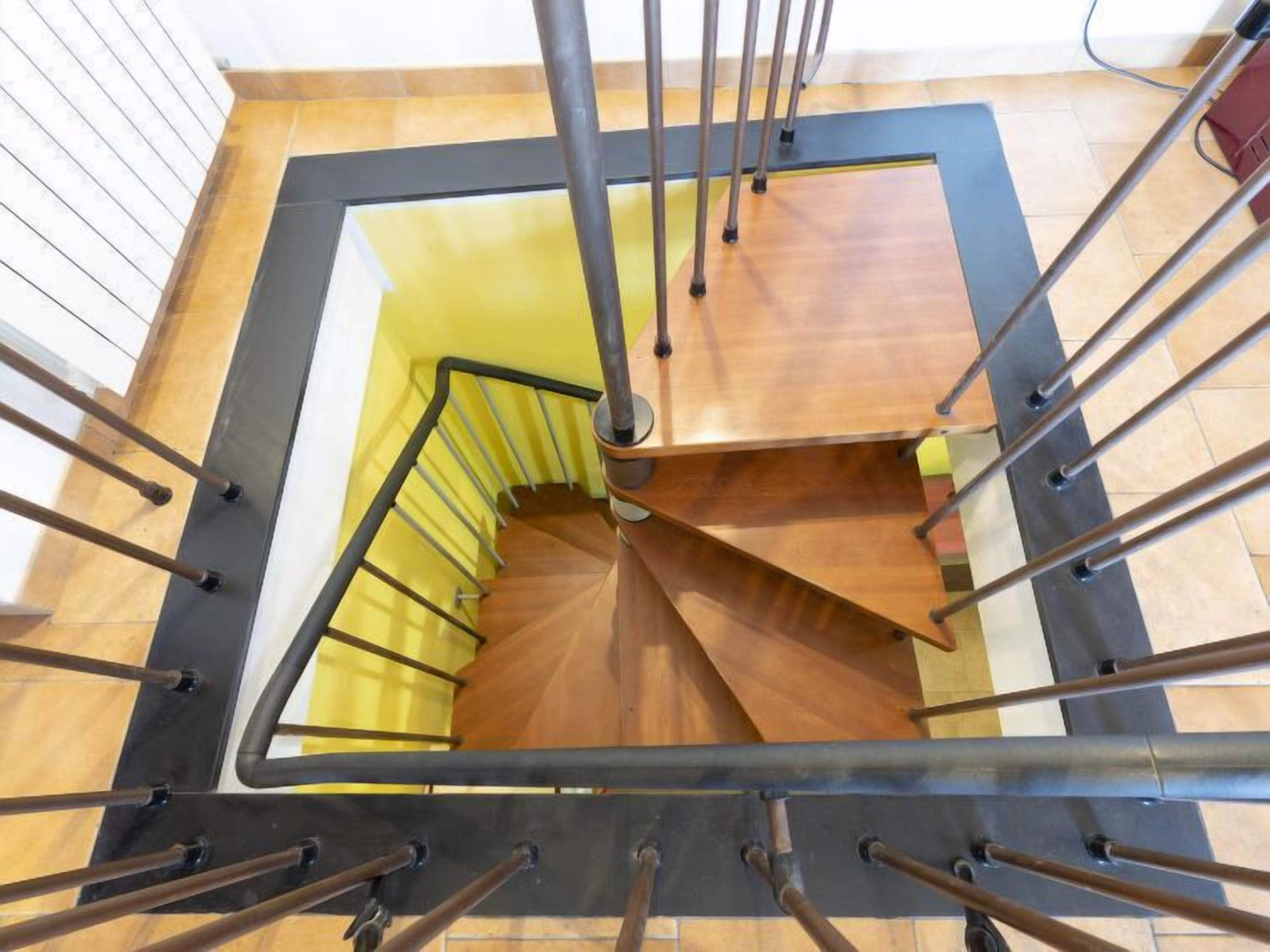 Un escalier en colimaçon avec des marches en bois et des rampes en métal, menant à l’étage supérieur.