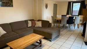 Uma sala de estar com sofá seccional, uma mesa de centro de madeira e um espaço de jantar com mesa e cadeiras.