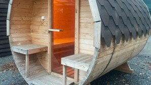 Uma sauna de madeira com telhado curvo, porta de vidro e duas fileiras de bancos de madeira.