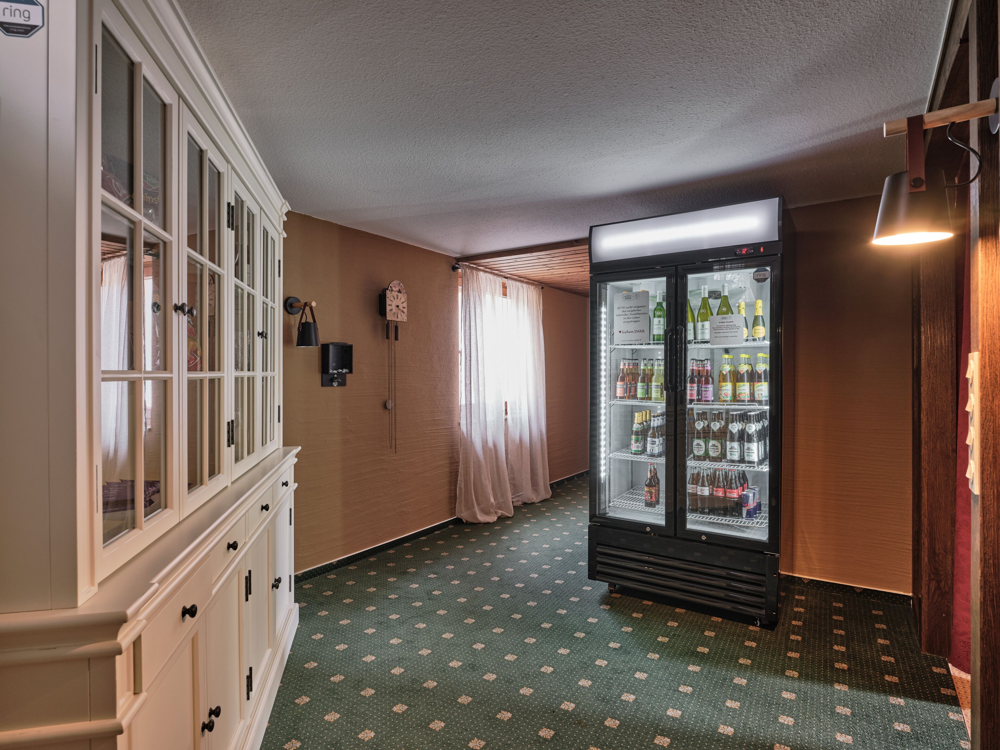 Un pasillo con un armario de madera, un reloj y un refrigerador lleno de bebidas.