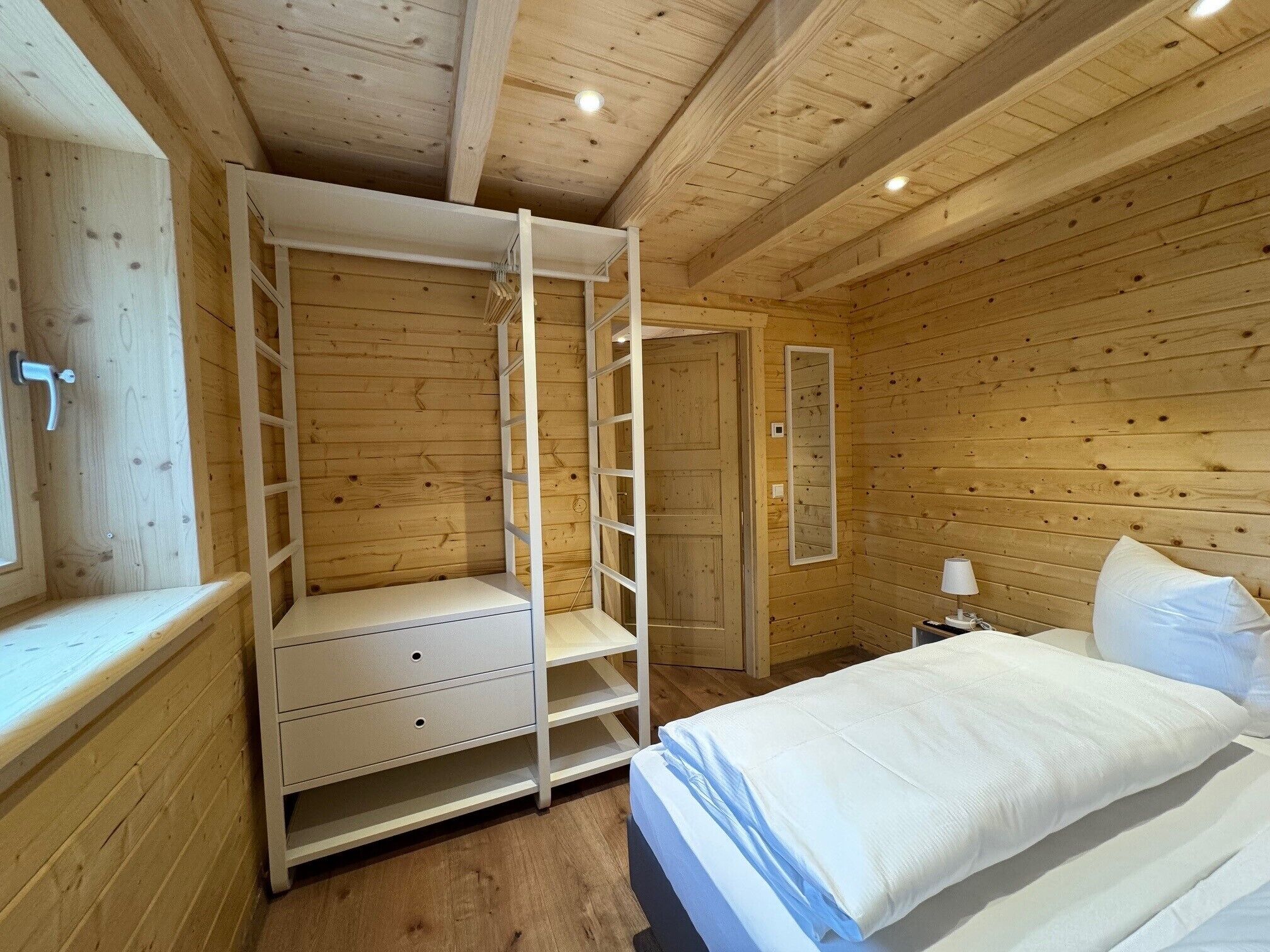 Een houten kamer met een bed, een witte kast en een spiegel aan de muur.