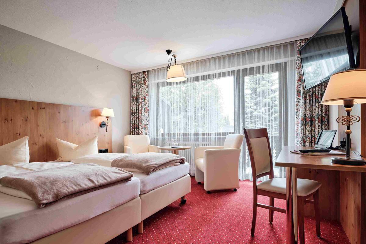 Habitación de hotel con dos camas, un escritorio con una computadora portátil, una silla y una ventana con cortinas.