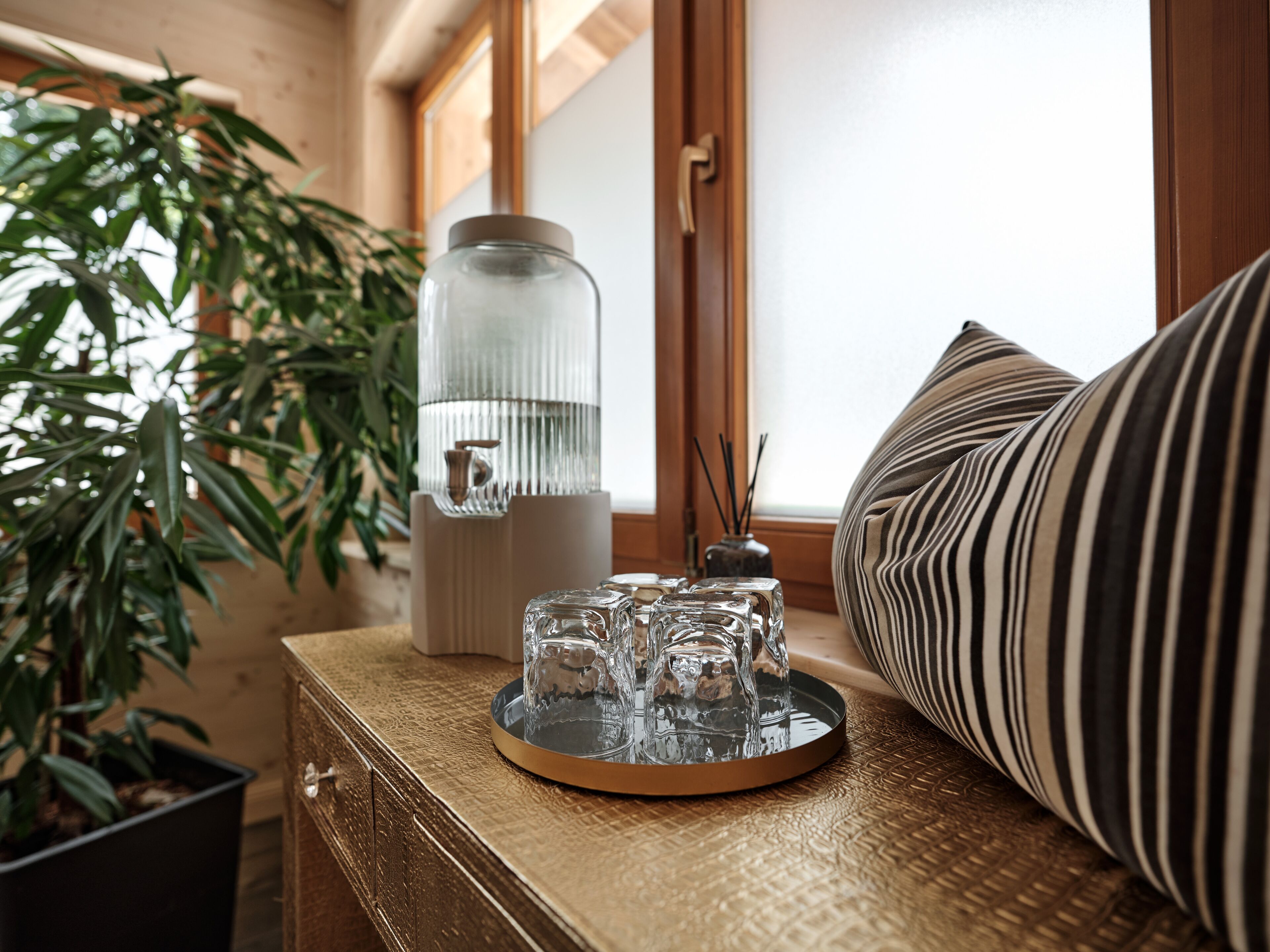 A wooden dresser with a glass jar, a tray with glasses, and a striped pillow.