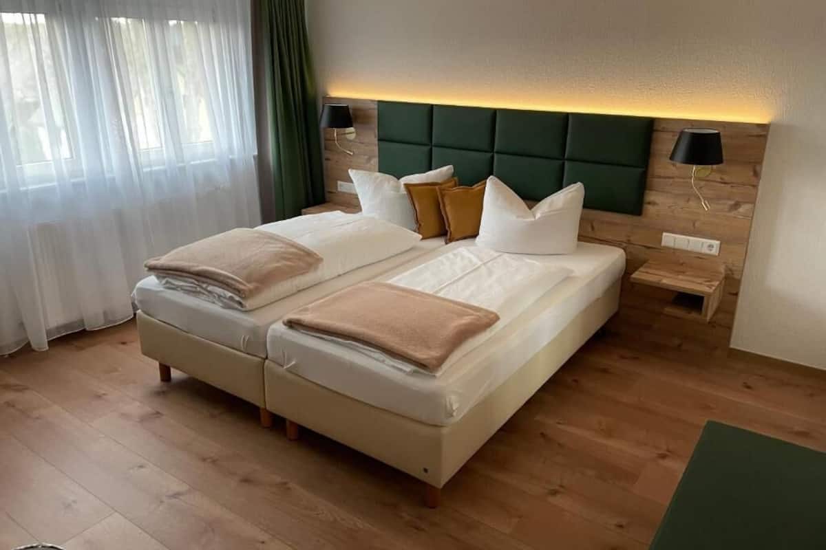 Una cama doble con cabecera, dos mesitas de noche, una cortina verde y suelo de madera.