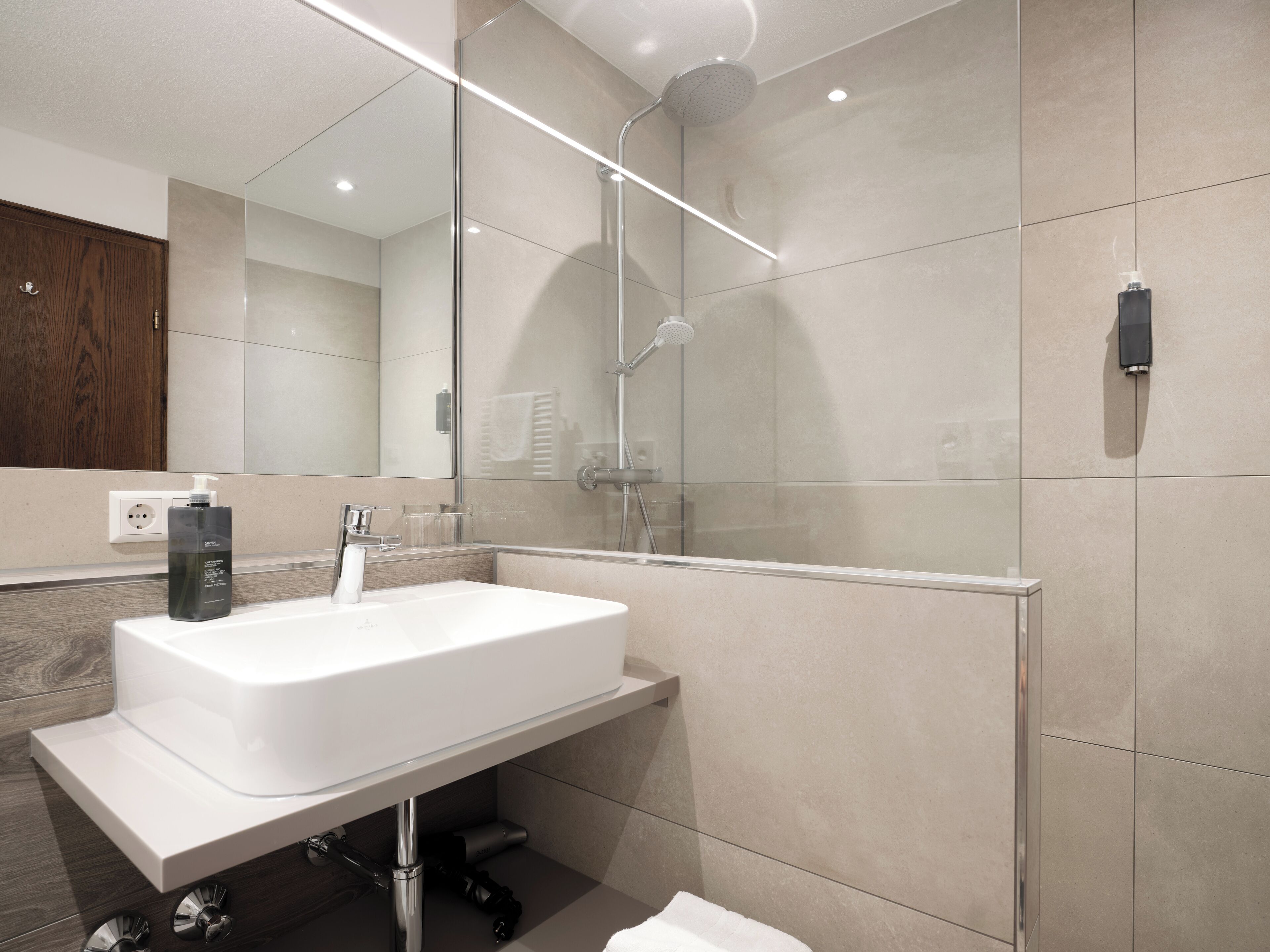 A modern bathroom with a large white sink, a glass shower enclosure, and a wooden cabinet.