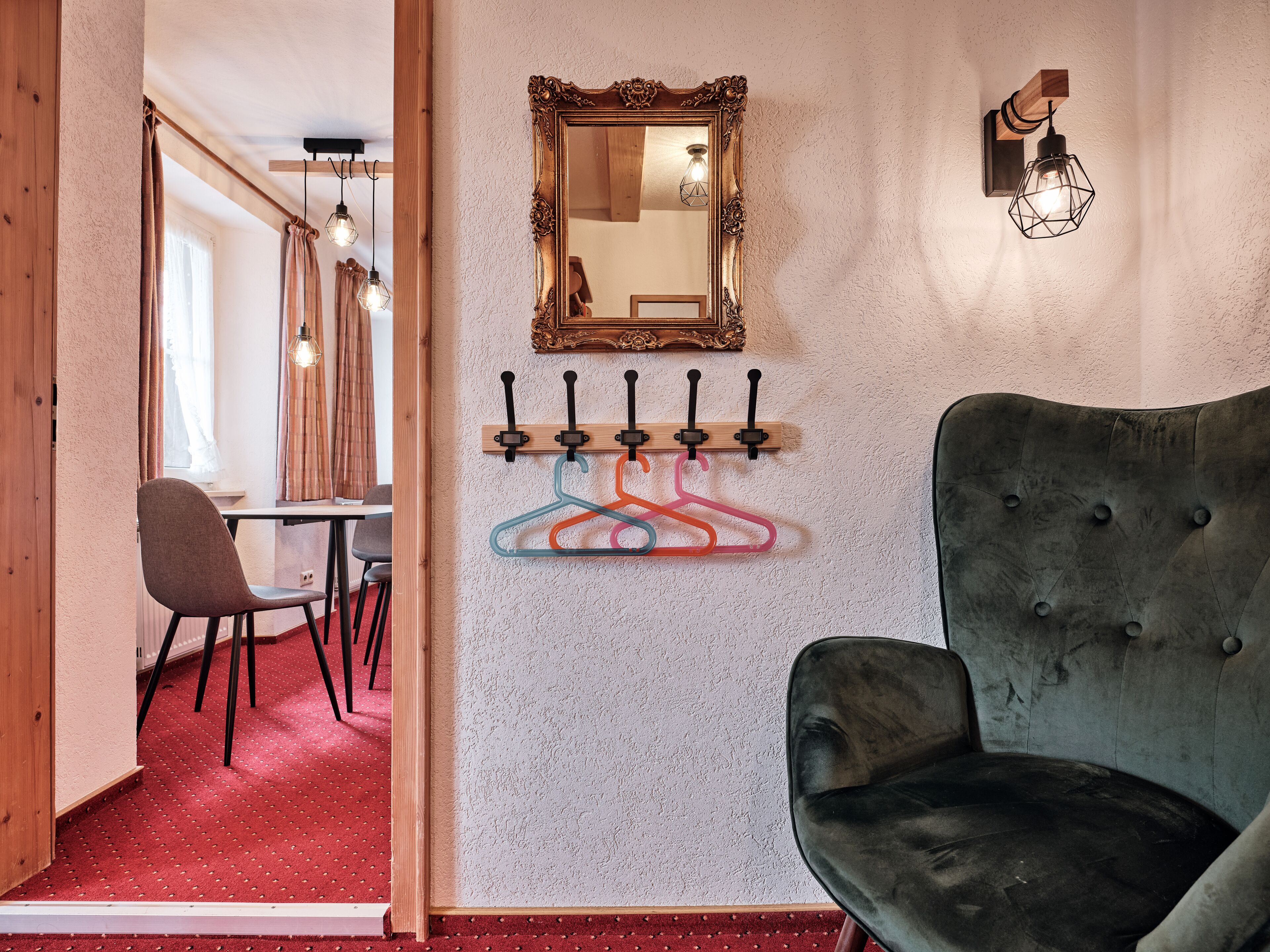 A room with a tufted armchair, a wall-mounted mirror, and a coat rack with colorful hangers.
