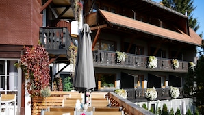 A wooden deck with tables and chairs, a balcony with flower boxes, and a building with a tiled roof. - Hotel Hochfirst (Lenzkirch)