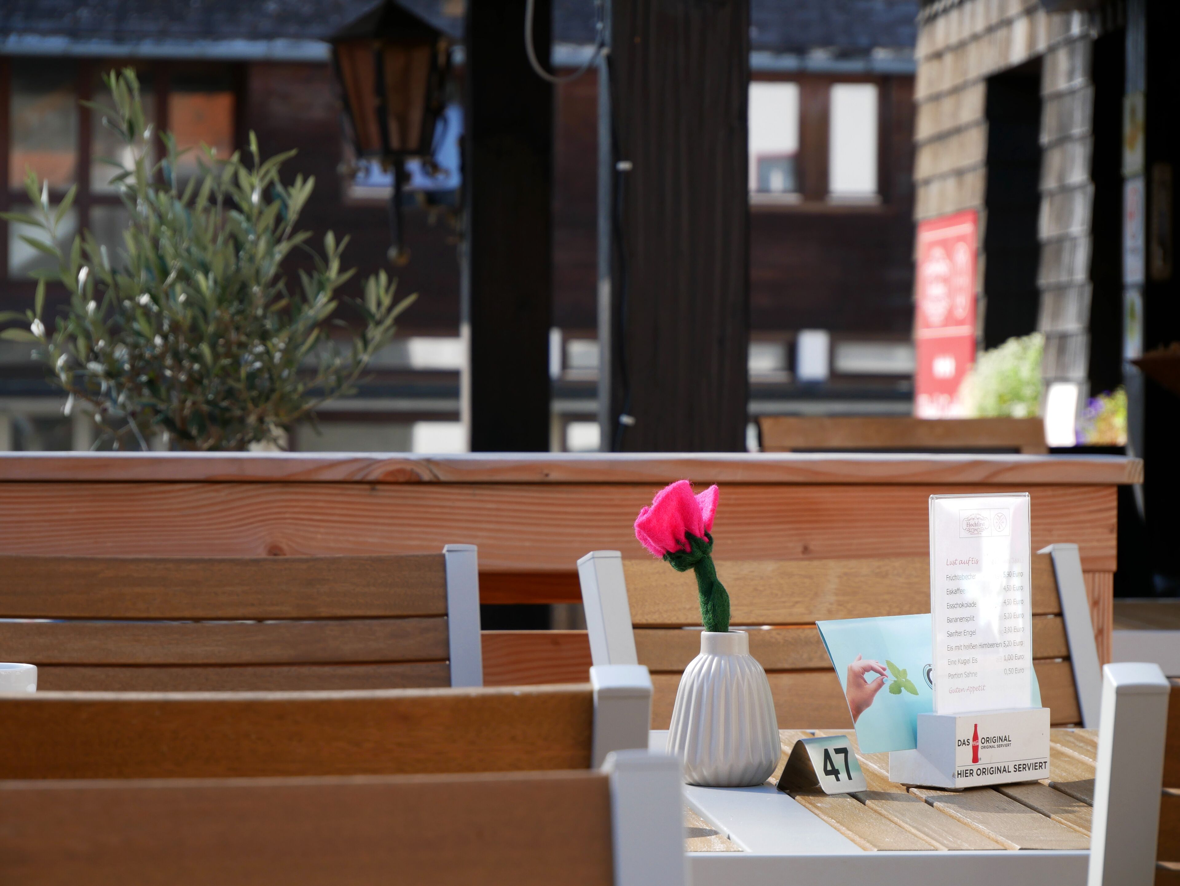 A wooden bench with a white vase containing a pink flower, a menu, and a small sign with the number 47.
