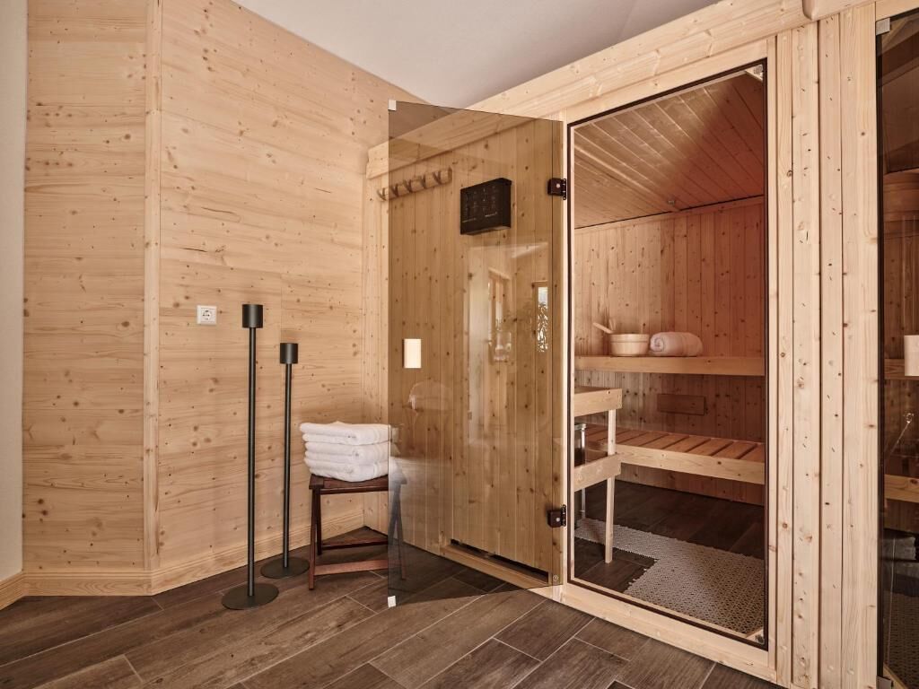 Uma sauna de madeira com porta de vidro, um porta-toalhas e um banco.