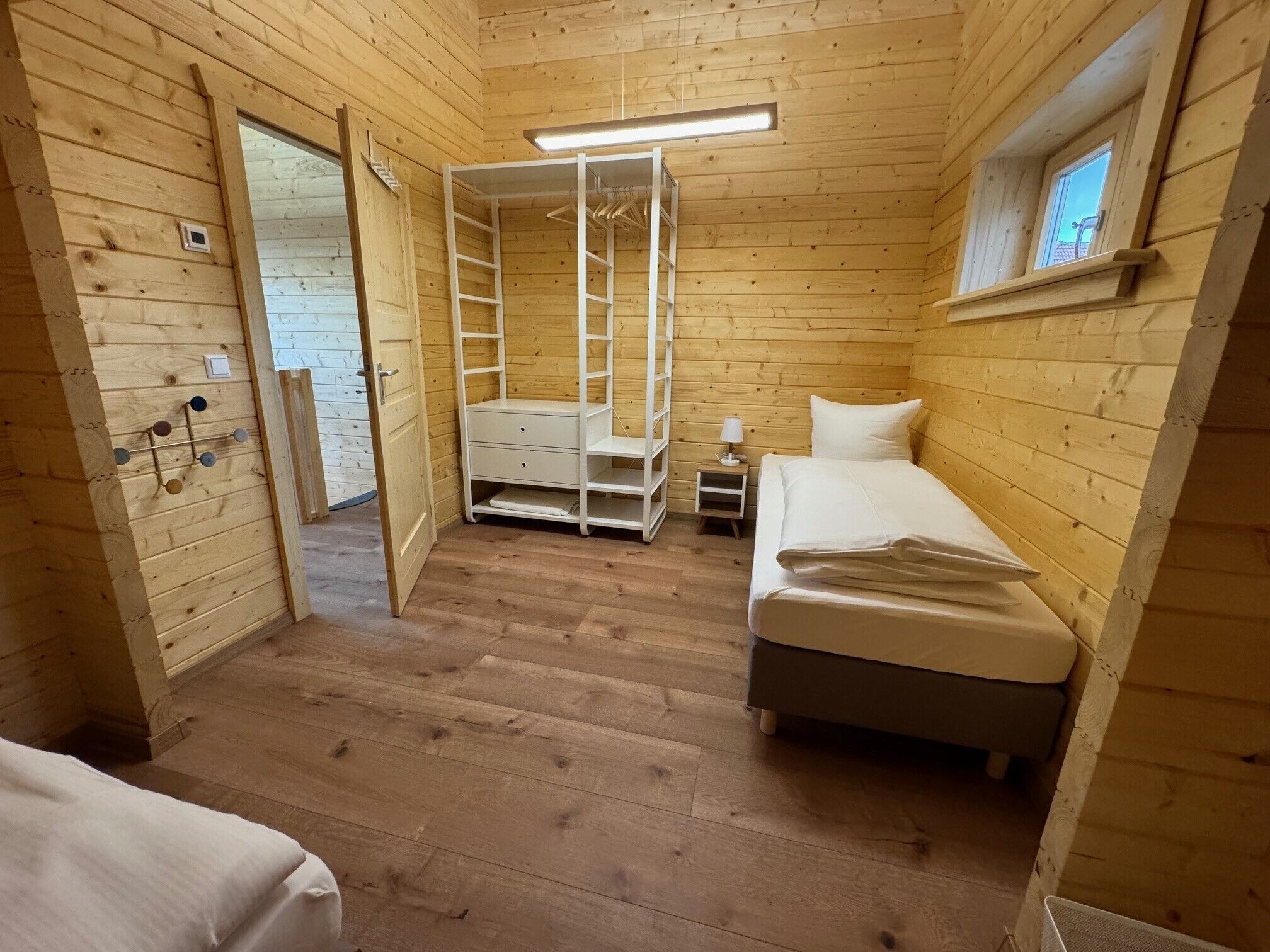 A wooden cabin room with a bed, a small bedside table, a wardrobe, and a window.
