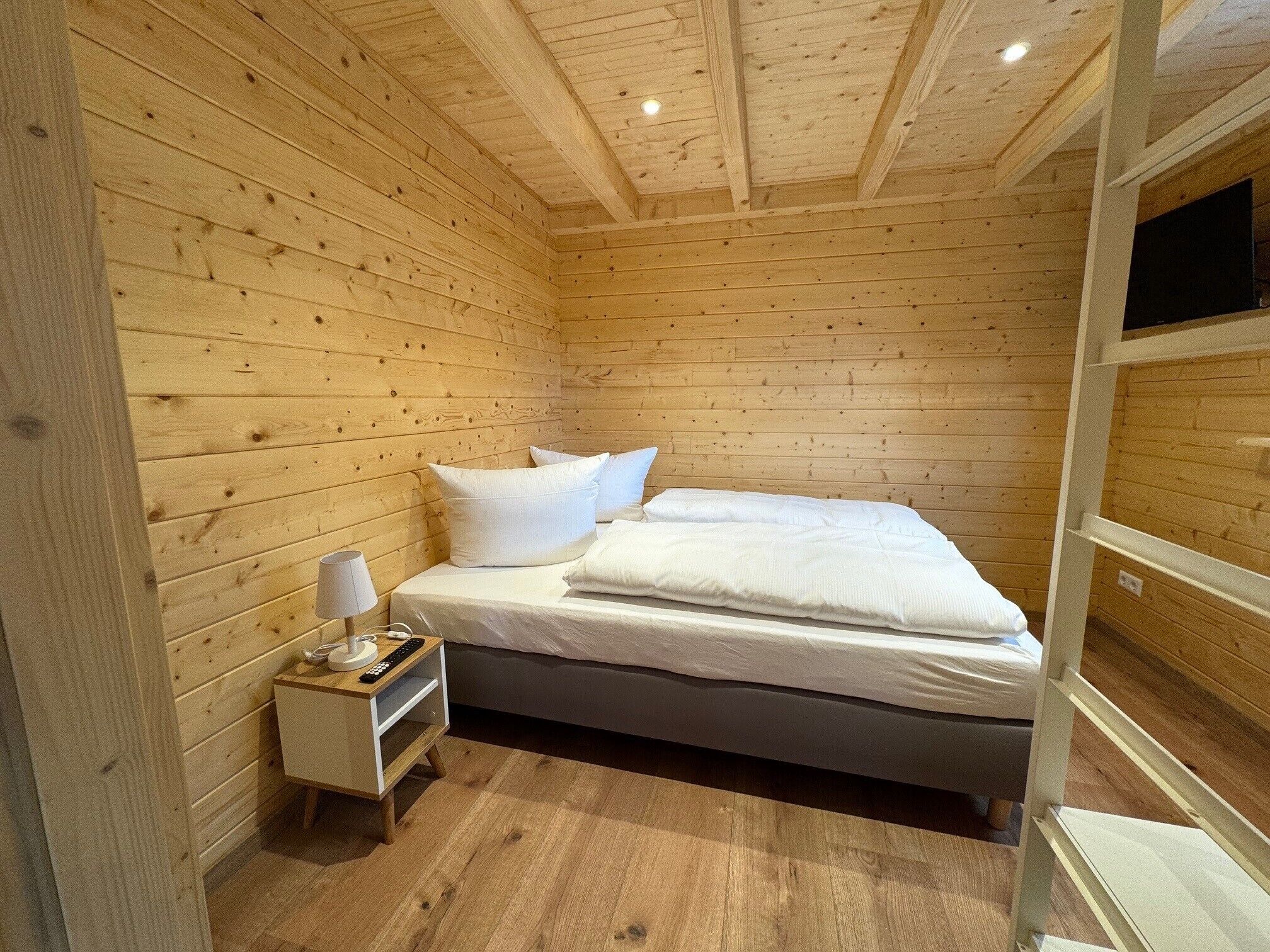 A wooden cabin room with a bed, a nightstand, and a lamp.