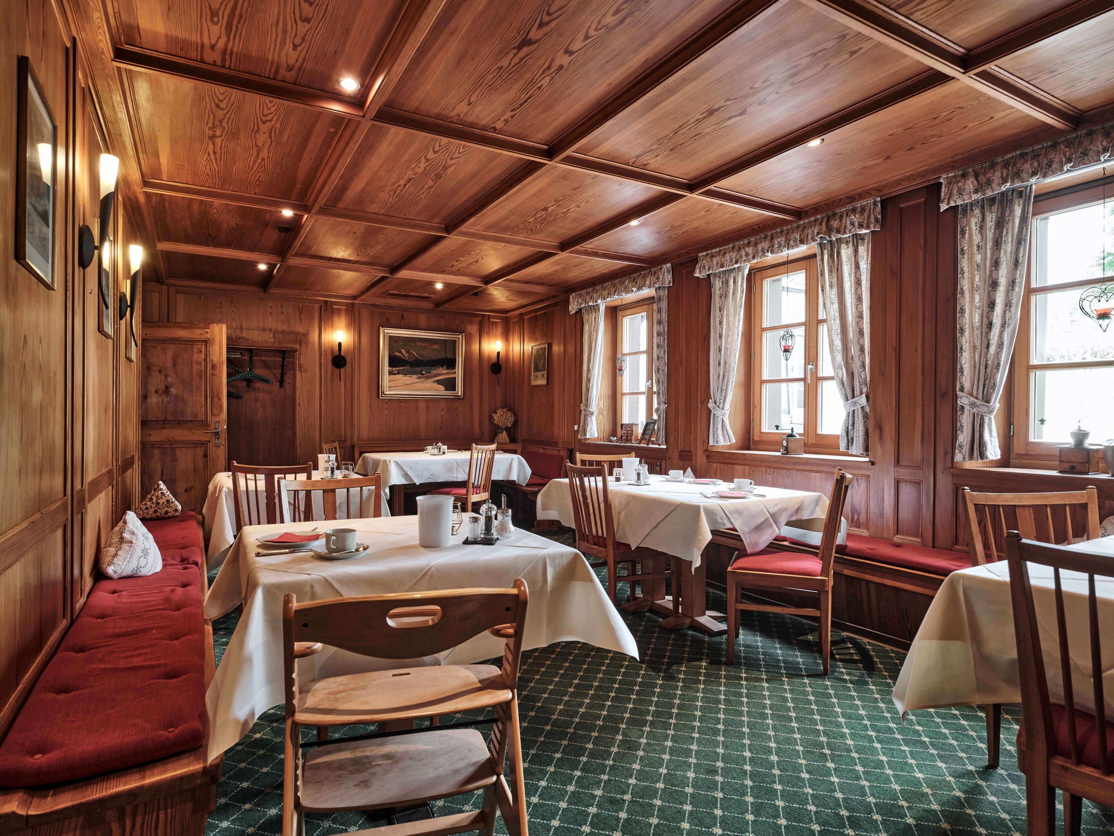 A wooden dining room with tables and chairs, a bench, and a patterned carpet.