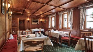 A wooden dining room with tables and chairs, a bench, and a patterned carpet.