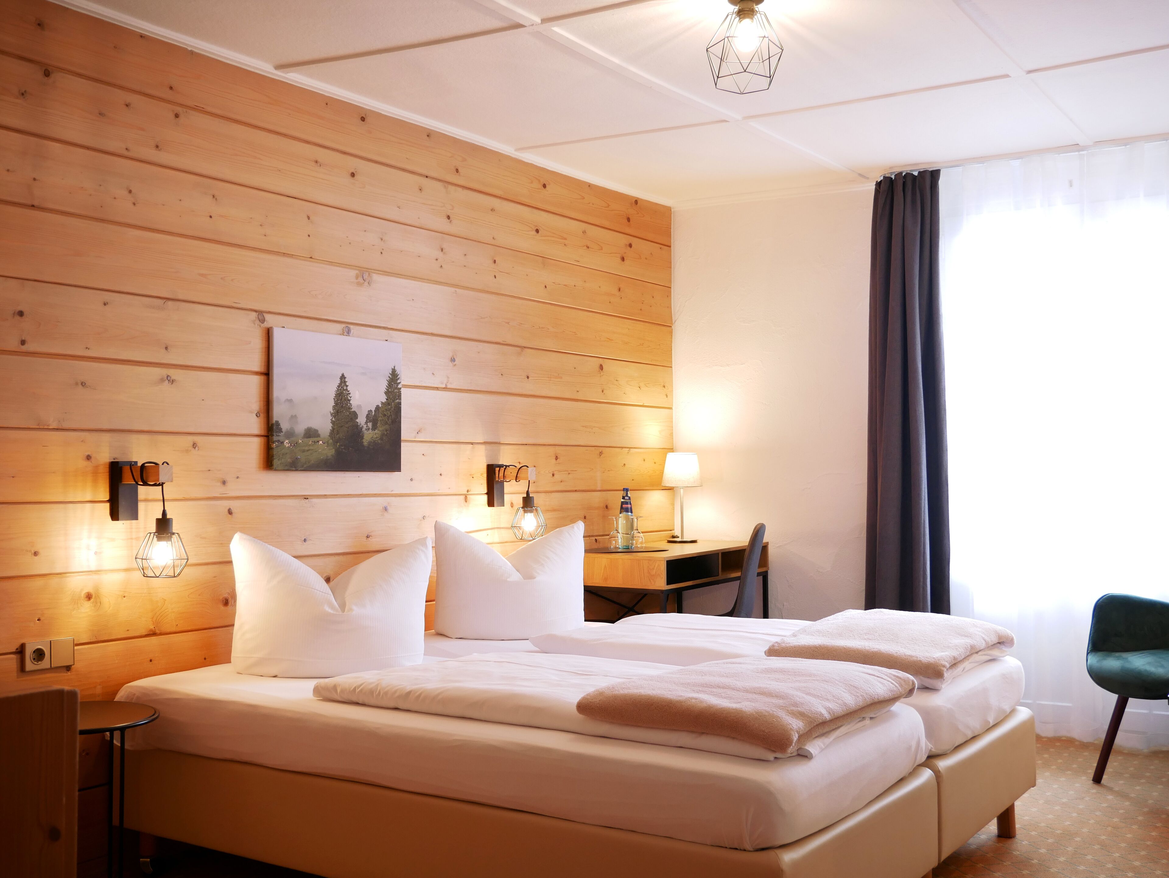 En dobbeltseng med hvide sengetøj, en træpanelfod, et skrivebord med lampe og en stol.