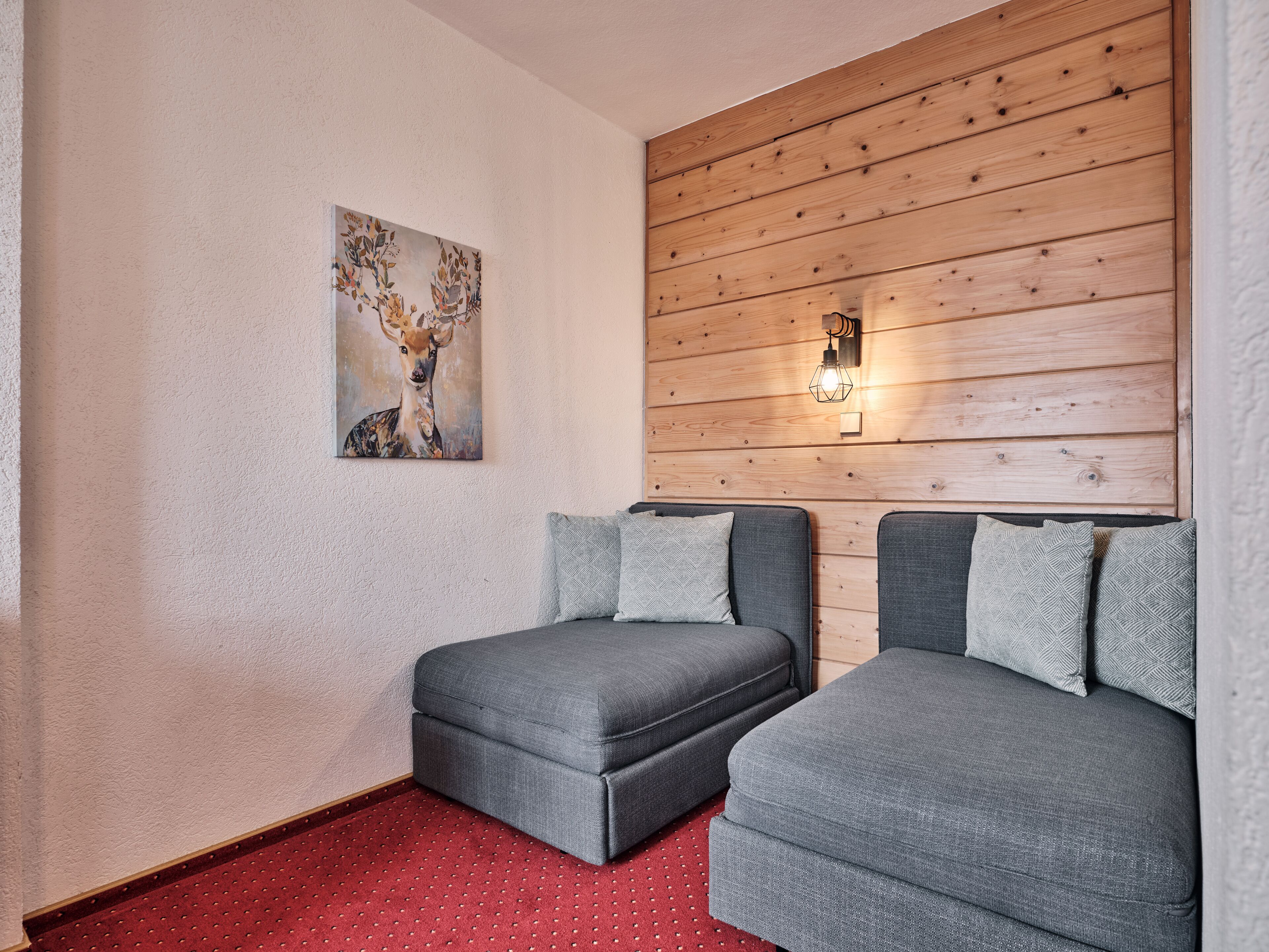 Una habitación con dos sofás grises, una alfombra roja, un panel de pared de madera y una lámpara de pared.