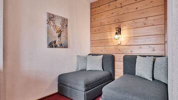 Una habitación con dos sofás grises, una alfombra roja, un panel de pared de madera y una lámpara de pared.