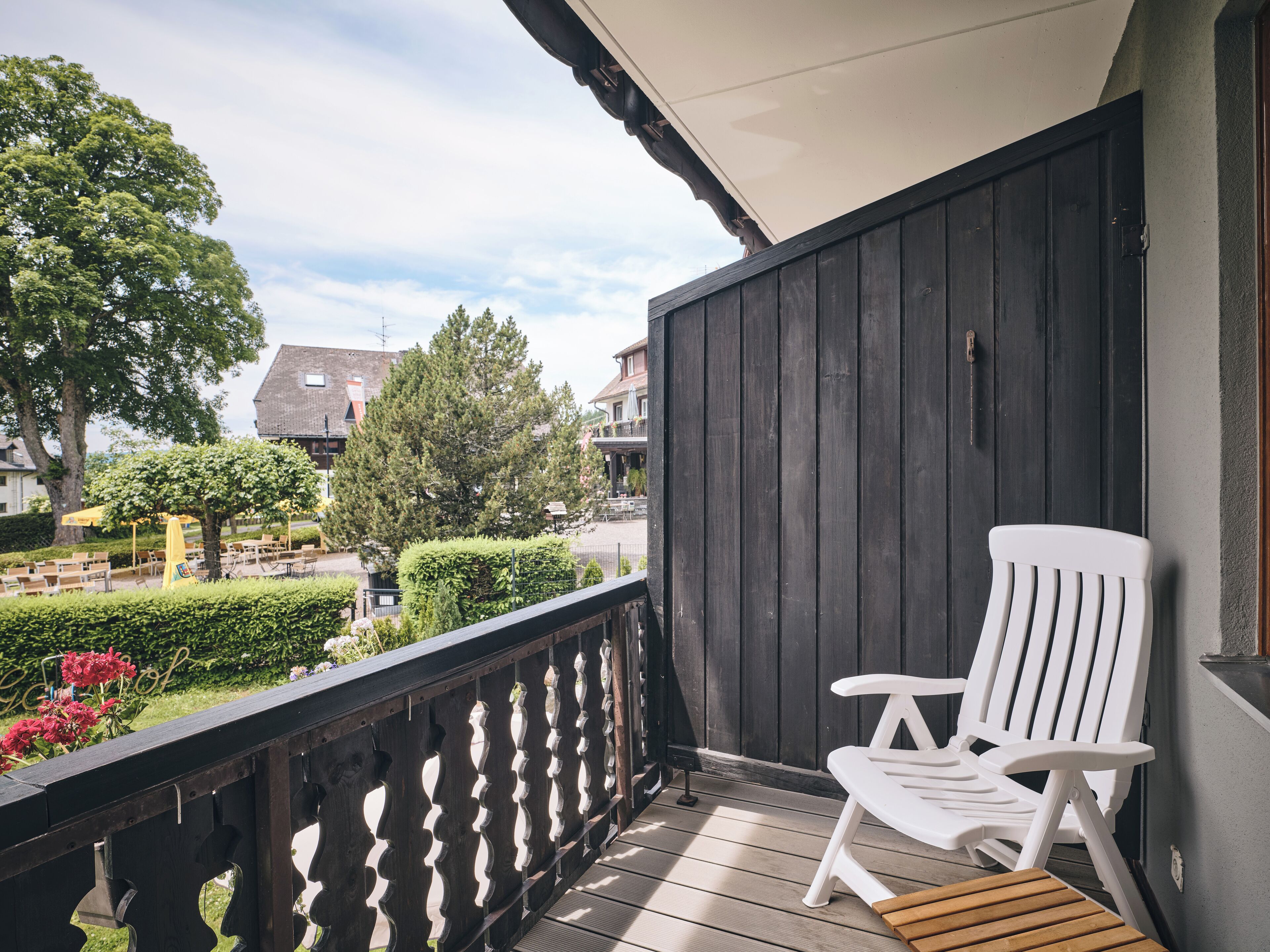 A wooden deck with a white chair, a wooden table, and a view of a town with buildings and trees.