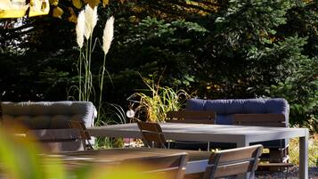 Un espace extérieur aménagé avec une table et deux canapés, entouré de verdure et d’arbres.