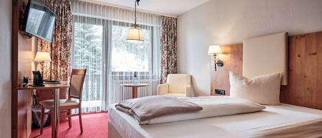 Ein Hotelzimmer mit einem Bett, einem Schreibtisch mit Stuhl, einem Fernseher, einer Lampe und einem Fenster mit Vorhängen.