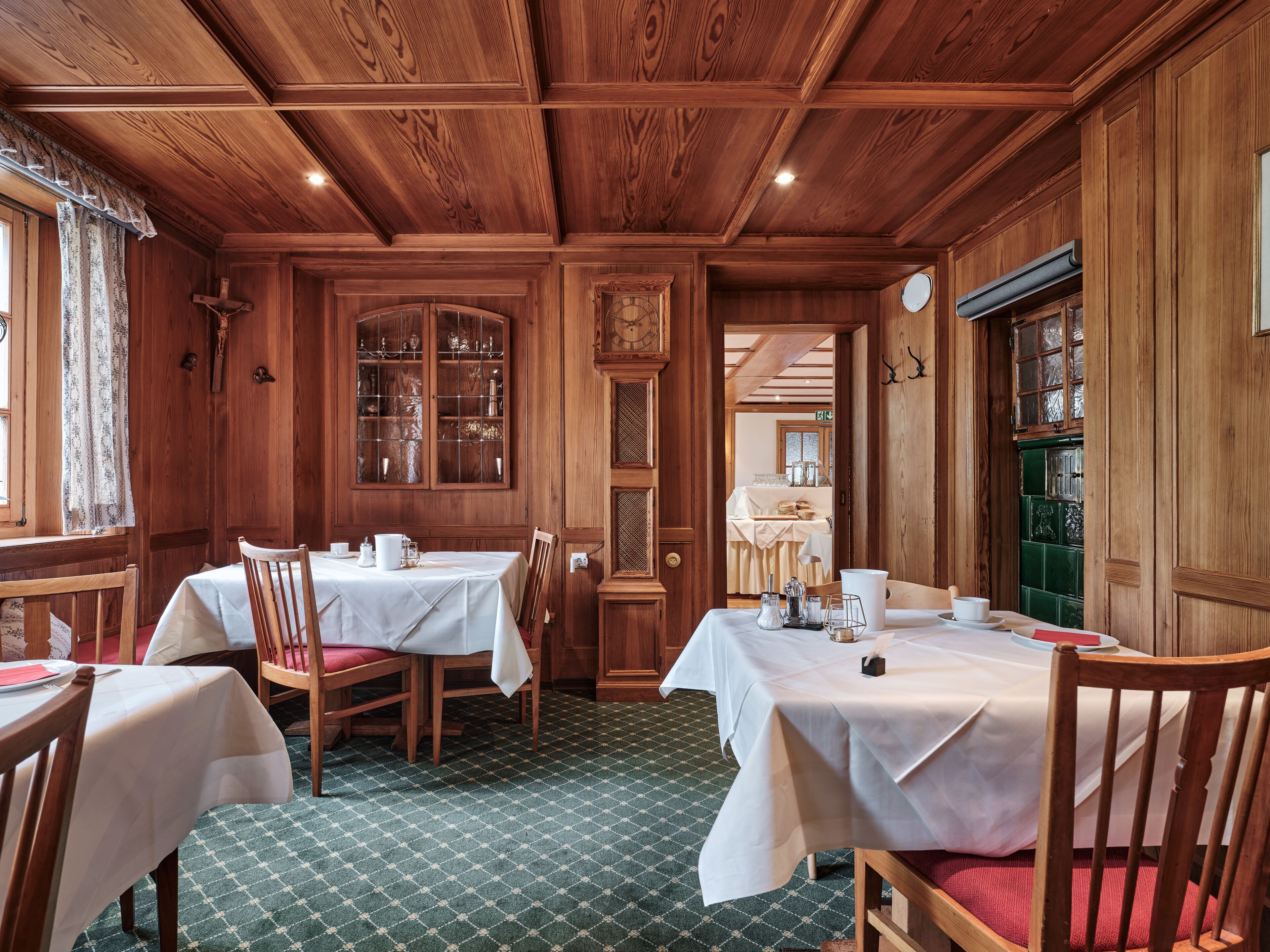 A dining area with wooden walls and ceiling, two tables with white tablecloths, and chairs.
