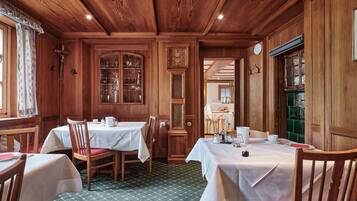 A dining area with wooden walls and ceiling, two tables with white tablecloths, and chairs.