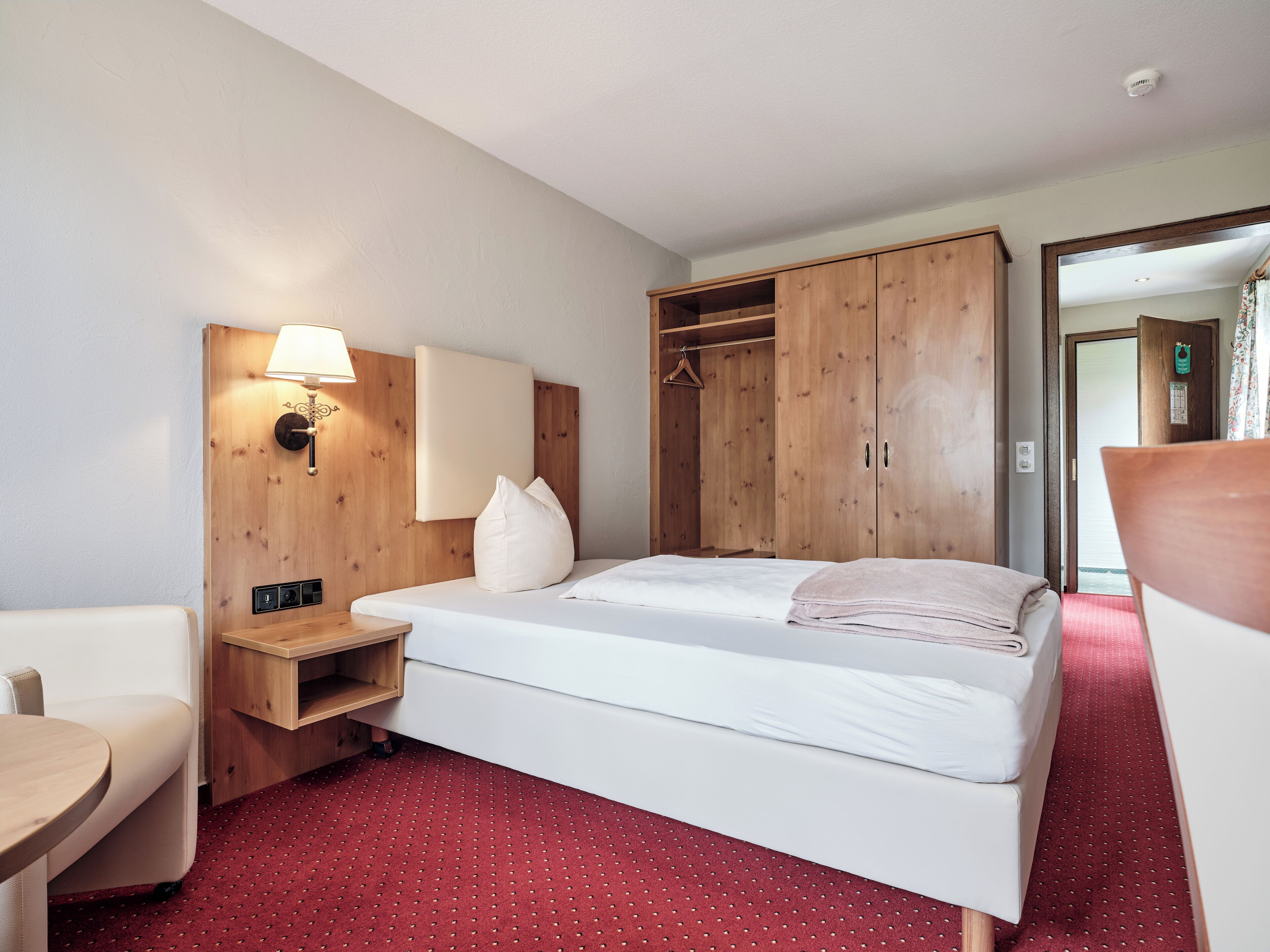 Et hotelværelse med en seng, et træskab, et natbord, en lampe og en stol.
