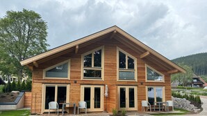A modern wooden house with large windows, a patio with chairs, and a view of the surrounding landscape. - Hotel Hochfirst (Lenzkirch)