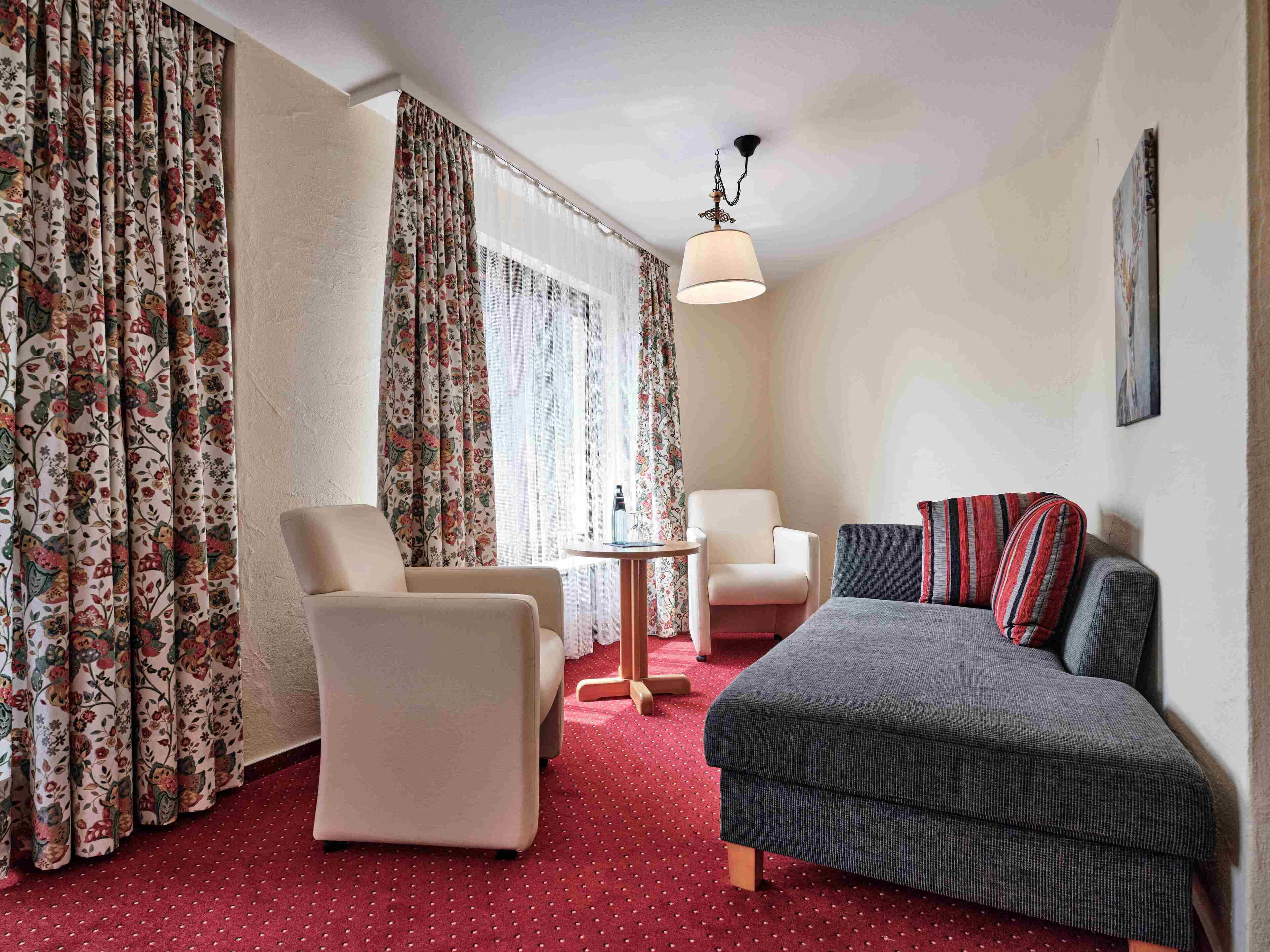 Habitación de hotel con sofá, dos sillones, una mesita y cortinas con estampado floral.